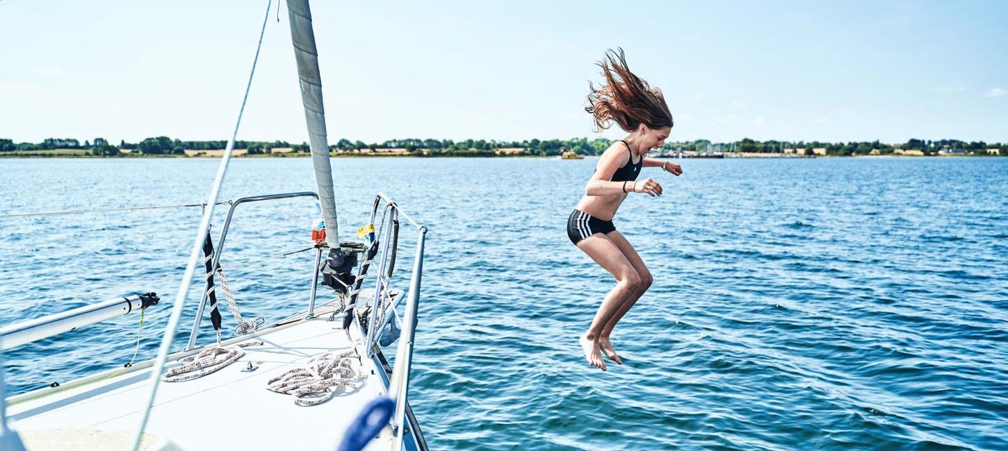 Pige midt i et hop fra båd. Det er sommer, havet er blåt og solen skinner.