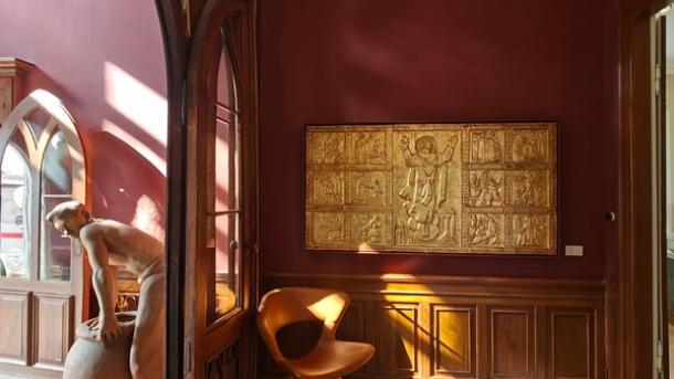 Et bordeaux indgangsrum med et kunstværk i guld hængende på væggen og en læderstol i hjørnet