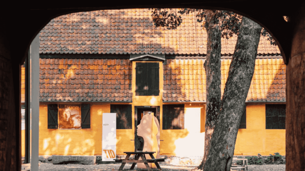 En gul gårdhave med bænk og et træ