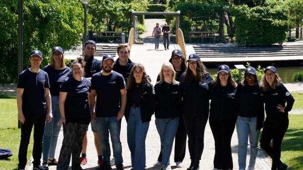 En gruppe turistguides i mørkeblåt tøj og kasketter står og smiler til kameraet.