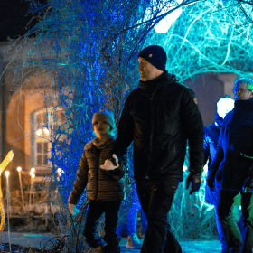 En familie går udendørs iklædt vinterbeklædning, og omkring dem er der lys i forskellige farver