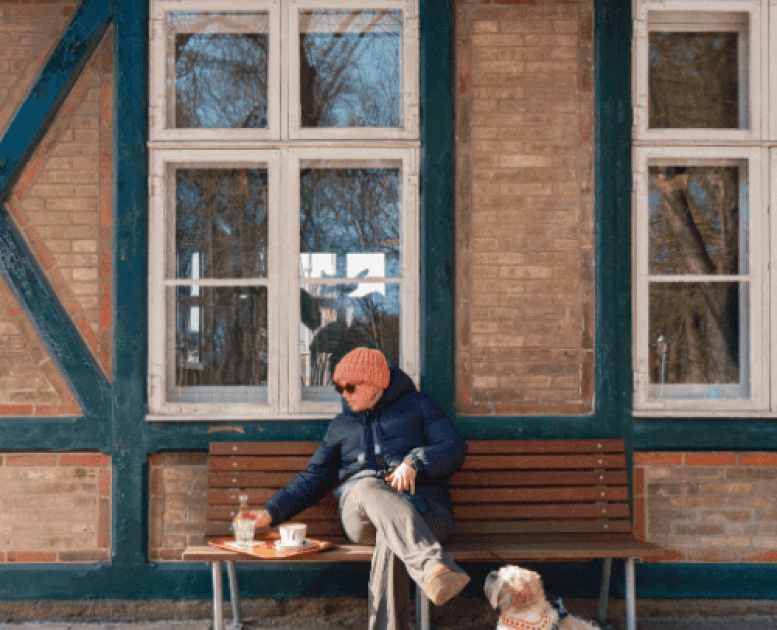 En kvinde iført vintertøj sidder ude foran en kaffebar med sin hund i snor og kaffe på en bakke