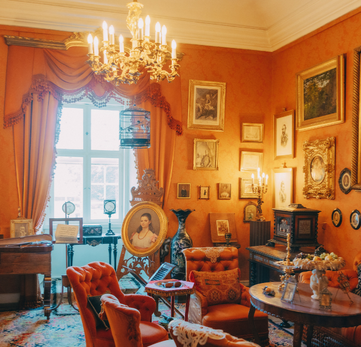 En stor dagligstue indrettet i renæssancestil med orangetonet interiør, lysekrone, tunge gardiner, stuk og massive møbler