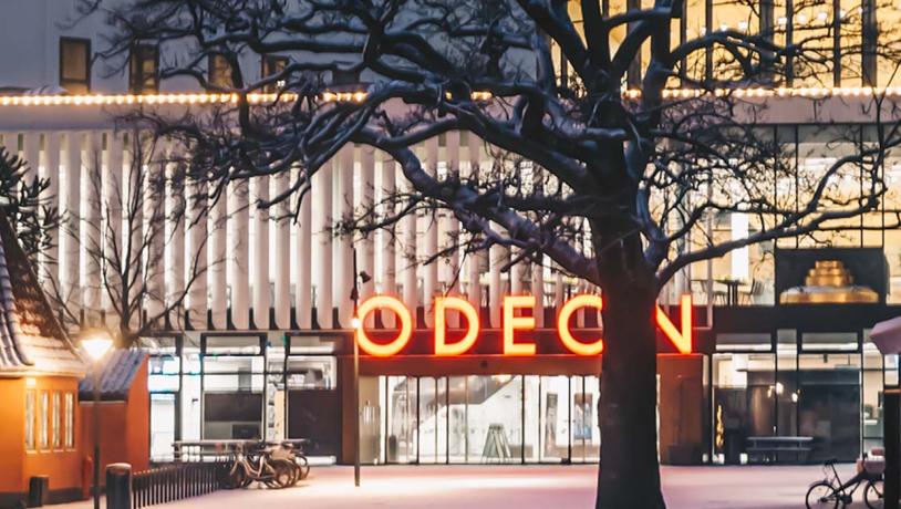 Odeon om aftenen set udefra foran hovedindgangen. Ovenover hovedindgangen er 'Odeon' oplyst med orange lys.