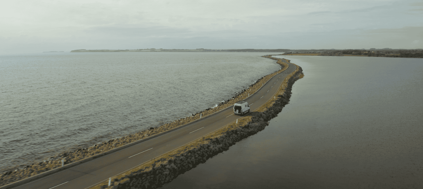 A white motorhome driving on a narrow dam with ocean to both sides