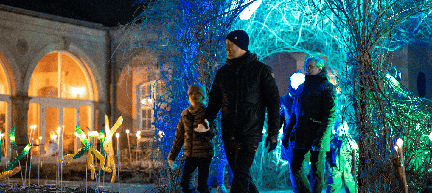 En familie går udendørs iklædt vinterbeklædning, og omkring dem er der lys i forskellige farver