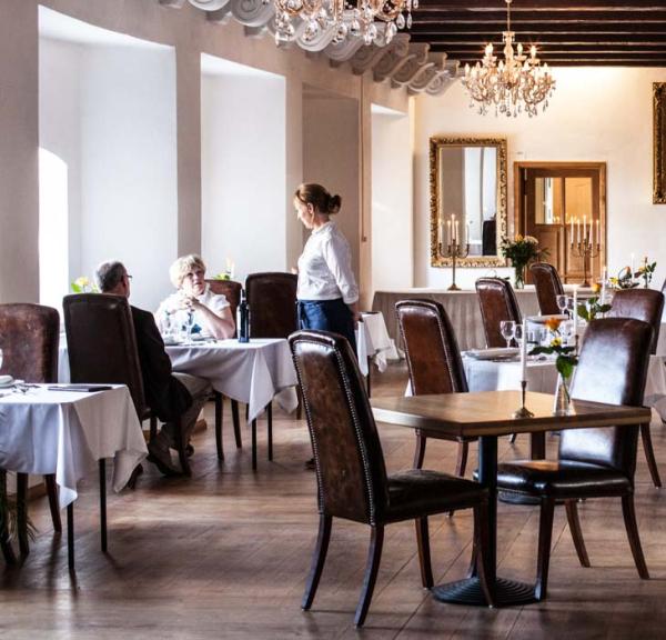 Stor, flot riddersal på en restaurant. Et par bliver serviceret ved en vinduesplads.